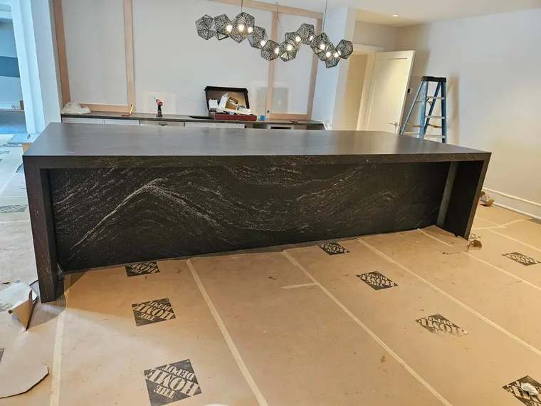 Custom basement entertaining bar with dark stone waterfall counter and sculptural chandelier